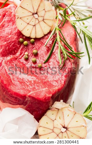 Raw beef meat with rosemary and garlic on white paper, ready for cooking, close up