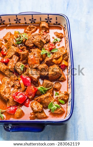 Beef goulash in casserole dish on light wooden background