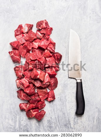 Raw beef goulash meat diced for stew with meat knife on light gray wooden background, top view
