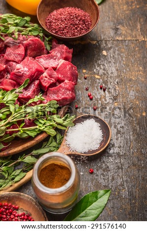 Raw meat cubes with herbs and spices. Goulash cooking preparation on rustic wooden background, place for text
