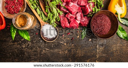 Ingredients for goulash or stew cooking: raw meat, herbs,spices,vegetables and spoon of salt on rustic wooden background, top view. Banner for website.