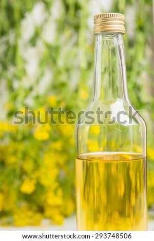 Glass bottle of rapeseed oil on rape blossoms background, close up
