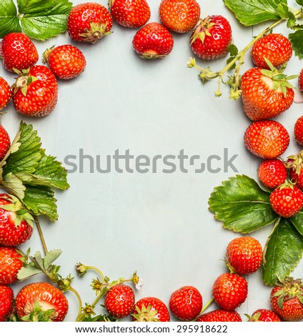 Frame of strawberries with green leaves and flowers on wooden background, top view, place for text