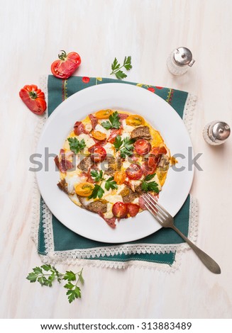 Country egg omelette in white plate with tomatoes,bread, cheese and sausage on wooden background, top view