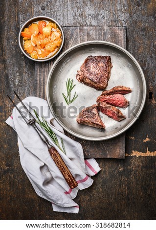 Sliced medium rare roasted beef steak, filet mignon , in metal rustic plate with meat fork and salsa sauce on dark wooden background, top view.