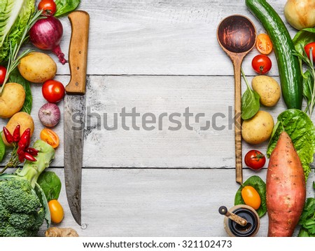 Delicious assortment of farm fresh vegetables with knife and spoon on white wooden background, top view. Vegetarian ingredients for cooking. Healthy cooking concept.