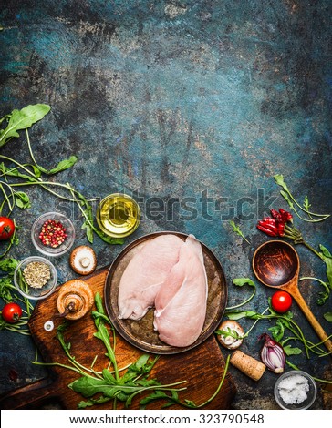 Chicken breast, wooden spoon and fresh delicious ingredients for cooking on rustic background, top view,frame. Healthy, diet food or Sports nutrition concept.