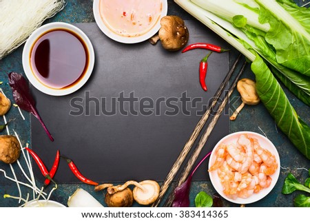 Chinese or Thai cooking food background. Asian food ingredients : soy sauce, chopsticks, rice noodles , pok choi,  shiitake mushrooms and scampi on black blank chalkboard, top view.