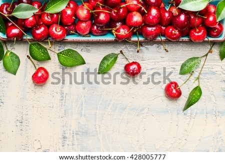 Border of sweet cherries with green leaves on light wooden background, top view, place for text. Summer fruits and berries concept.