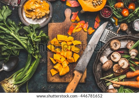 Chopped Pumpkin on rustic cutting board with kitchen knife and mushrooms and vegetables ingredients  for tasty vegetarian cooking, dark styled,  top view