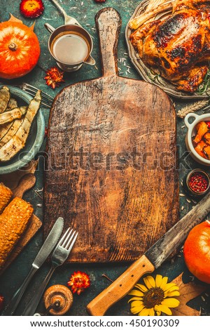 Roasted whole chicken or turkey, pumpkins, corn and harvest vegetables with kitchen knife and cutlery served around aged wooden cutting board on dark rustic background, frame. Thanksgiving Day food