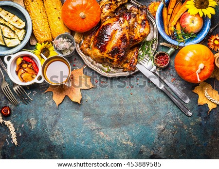 Festive  Thanksgiving Day food background with roasted whole turkey or chicken and sauce, harvest vegetables: corn, pumpkin,carrots with cutlery on dark rustic kitchen table, top view, border