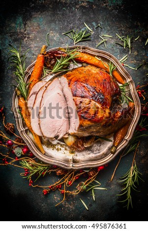 Roasted sliced pork ham and roast vegetables on dark rustic background, top view