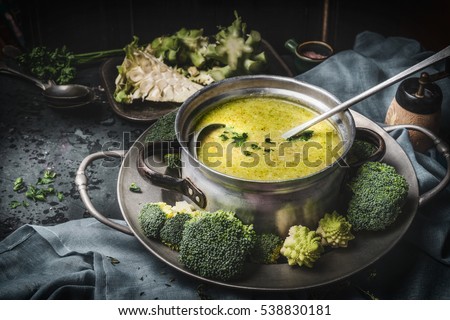 Cooking pot with green romanesco and broccoli soup and ladle on dark rustic kitchen table . Healthy food and diet nutrition concept.