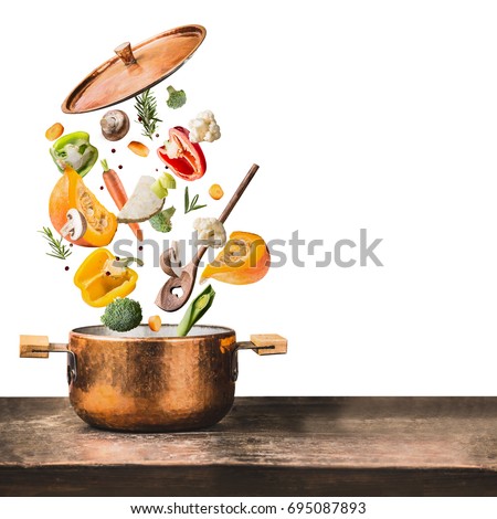 Healthy vegetarian eating and cooking with various flying chopped vegetables ingredients, cooking pot and  spoon at wooden table desk , isolated on white background, front view. Clean food concept