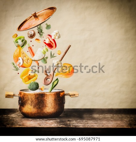 Healthy vegetarian eating and cooking with various flying chopped vegetables ingredients, cooking pot and  spoon at wooden table at natural background, front view. Clean food concept