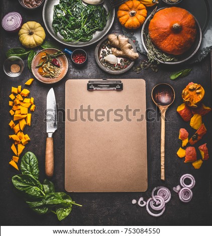 Food background for tasty winter and autumn dishes with pumpkin. Various cooking ingredients with spoon and knife around blank cardboard clipboard for menu or recipes , top view, frame, mock up