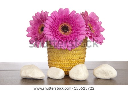 Pink Gerbera in yellow straw basket behind four white stones on a dark brown wooden shelf