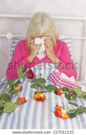 Sad woman in pink pajama sitting in bed with a bunch of roses and tissues