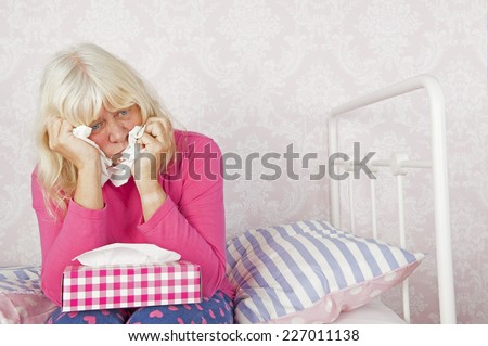 Sad woman with pink pajama and tissues sitting on edge of bed