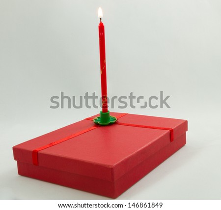 A lit red candle in a green candle holder on top of a red gift box