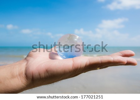 hand holding glass globe with beautiful beach view background