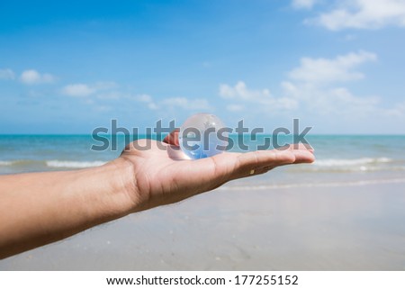 hand holding glass globe with beautiful beach view background