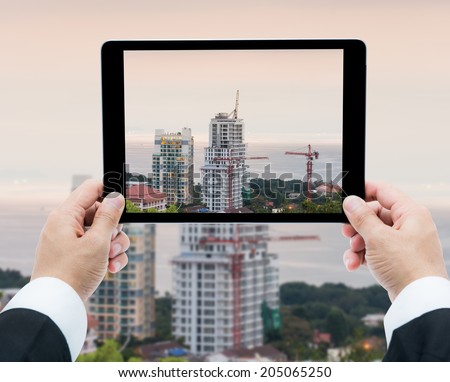 Businessman hands tablet taking pictures buildings under construction and cranes the sea