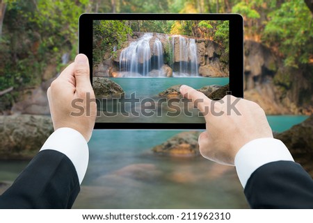 Businessman hands tablet taking pictures Waterfall deep forest  at Erawan waterfall National Park Kanchanaburi of Thailand