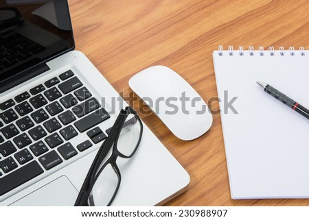 Blank business laptop, mouse, pen, note and glasses on wooden table