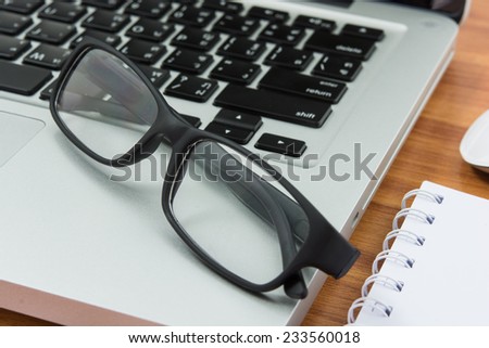 Blank business laptop, mouse, pen, note and glasses on wooden table