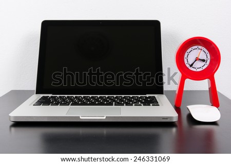 Laptop and red clock  on black wooden table on wall background