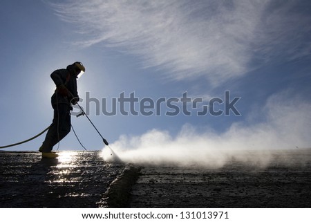 Worker on top of factory hall, with high pressure washer, cleans layer of old concrete