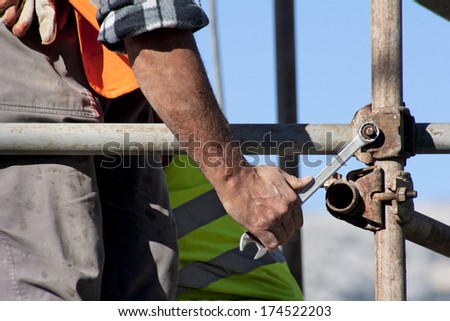 Worker with wrench in his hand builds iron scaffold on construction site