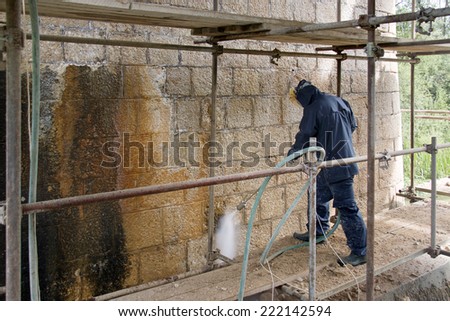 Construction worker cleaning dirtiness with high pressure washer from ancient stone wall