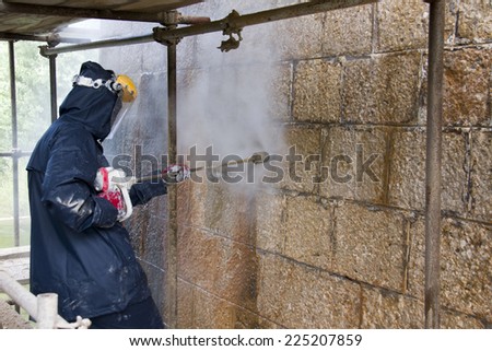 Construction worker cleaning dirtiness with high pressure washer from ancient stone wall