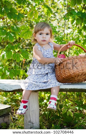 little girl sits on a bench with a basket of apples