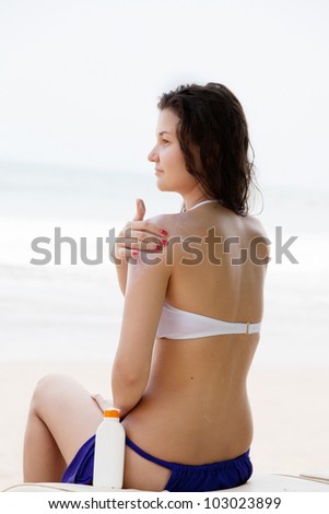 girl on a beach puts sun-protection cream on skin