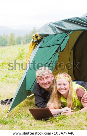 Happy pair in tent works on a laptop against mountains