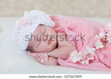 newborn girl sleeps with spring flowers under a knitted pink cape