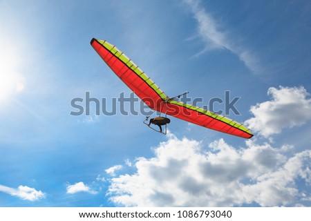 The hang glider on a red hang-glider is flying in a blue sky