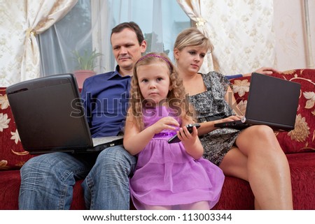 Parents and the child have a rest on a sofa, everyone with the personal computer