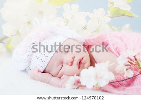 newborn girl sleeps with spring flowers under a knitted pink cape