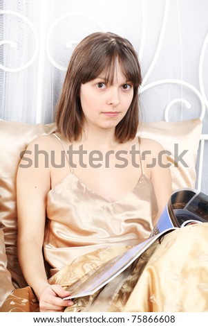 beautiful girl reads magazine lying in a bed