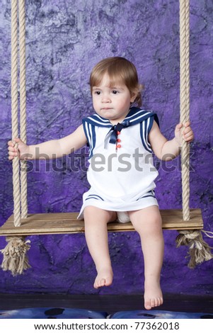 little girl in a dress in sailor's style sits on a rope swing. Studio shooting.