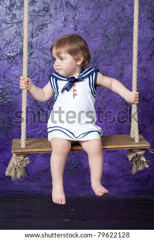 little girl in a dress in sailor\'s style sits on a rope swing. Studio shooting.