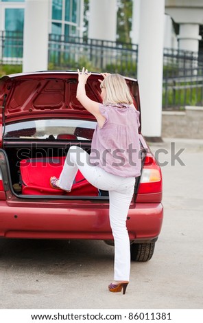 girl stacks a suitcase in a car luggage carrier