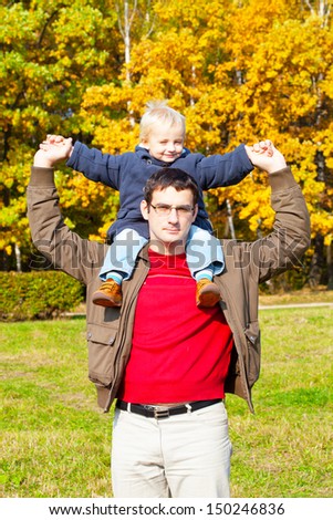 small son sits on shoulders at the father. Walk in autumn park in solar weather