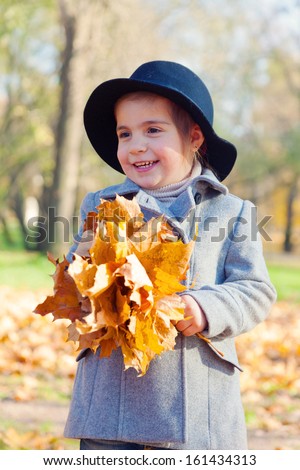 child the girl in a coat and a hat to stand with a bouquet of maple leaves