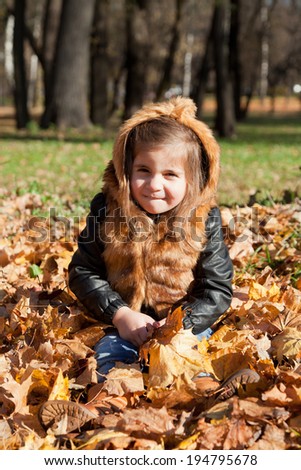 girl in a fur jacket sits on the fallen-down autumn leaves